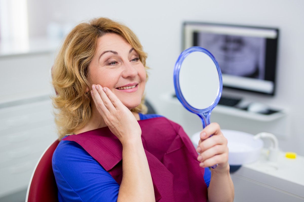 Woman examining her smile in handheld mirror at dental office