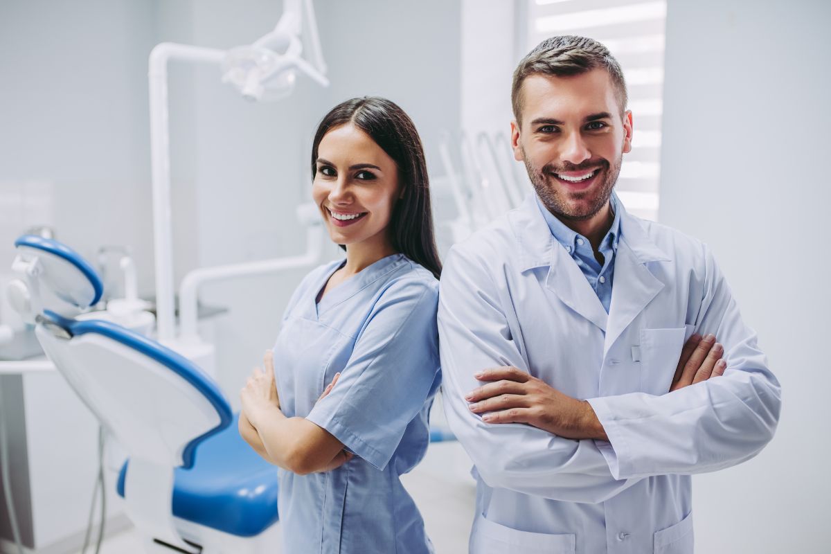 Two dental professionals in white coats smiling in modern dental office with equipment.