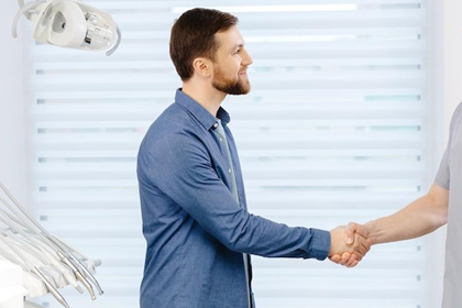 Male patient shaking hands with dental professional in modern dental office treatment room.