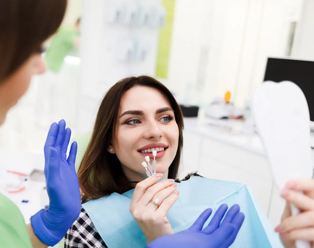 Dental hygienist wearing blue gloves examines patient's teeth in clinical office setting.