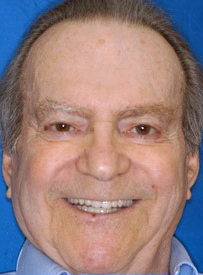 Middle-aged man smiling at camera against blue background, professional headshot for dental practice.