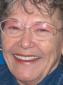 Smiling woman wearing glasses and blue shirt, professional headshot for dental care practice.