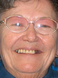Close-up portrait of smiling middle-aged person wearing clear-framed glasses against blue background.