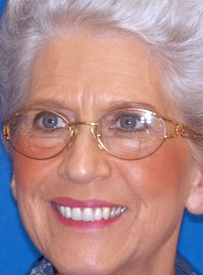 Senior woman wearing glasses smiling at camera against blue background for dental care website.