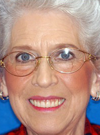 Smiling woman wearing glasses and red clothing against blue background, dental care professional portrait.