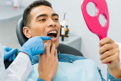 Dentist examining patient's teeth in clinical setting with mirror and gloved hands.