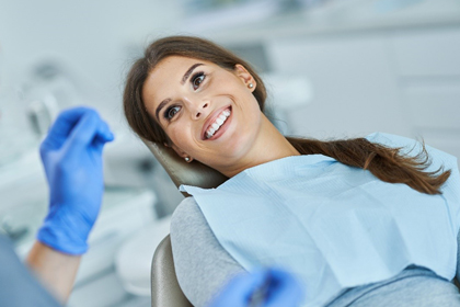 Smiling female dentist in blue gloves and mask giving thumbs up in dental office.