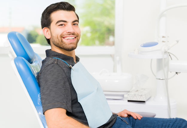 Smiling male patient seated in blue dental chair at modern dental office