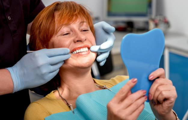 Woman receiving dental examination from dentist in clinical office setting, holding mirror.