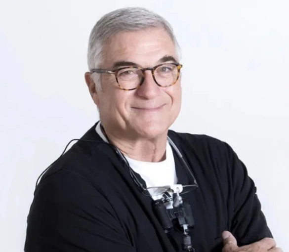 Professional headshot of middle-aged man with gray hair and glasses wearing black cardigan over white shirt, smiling at camera against white background.