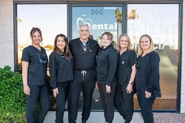 Dental team of six professionals in black scrubs posing outside practice entrance in Sun City West.